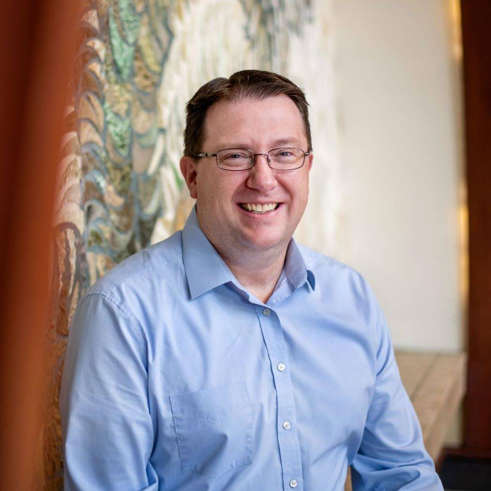 Neal Buckwalter sitting in front of mural in DeVos Building